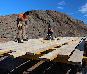 Nev and Rohan nail the wood planks onto the deck.