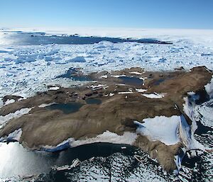 An island with a number of buildings are seen by air. Buildings on the left belong to the Chinese station Zhongshan. Buildings on the right side of the island belong to Russian station Progress. The island is surrounded by packice and icebergs.