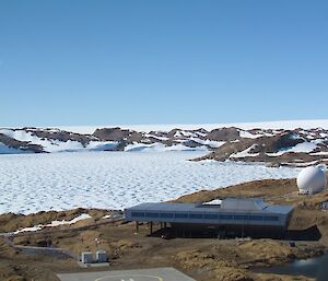 A very modern, rectangular building is seen from the air. It is close to the island edge. Sea ice is seen in the background.
