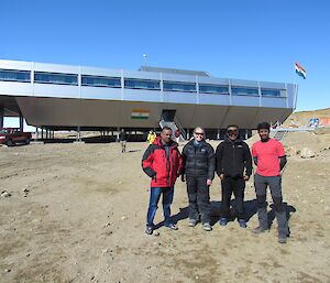 Three Australian expeditioners stand with the Indian station leader for a photo in front of the Bharati station building.