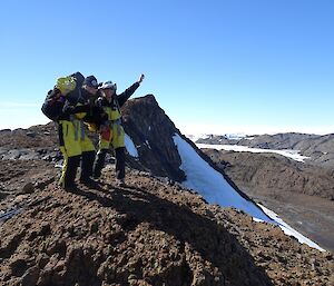 Two expeditioners on a lookout point wearing heavy packs. Below them are the rocky valleys of the Vestfold Hills.
