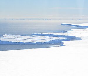The Antarctic plateau meets the ocean. A large iceberg, recently broken off from the iceshelf is visible.