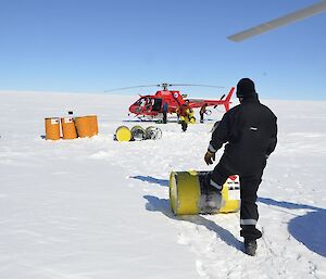 Two helicopters have landed on the plateau. People are moving around yellow and orange fuel drums, positioned between the two helicopters.