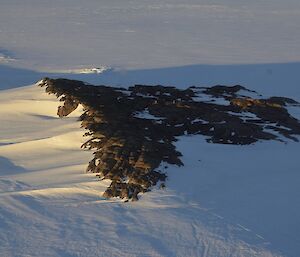 An aerial shot of a small, triangular outcrop of rocks, on the icy Antarctic plateau.