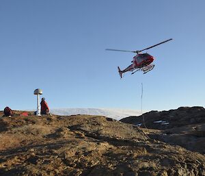 A helicopter slings drums of fuel onto rocky land for future supplies.