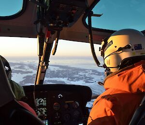 Inside the helicopter, looking past the pilot to the Vestfold Hills. There is a soft pink, midnight light.