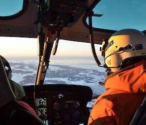 Inside the helicopter, looking past the pilot to the Vestfold Hills. There is a soft pink, midnight light.