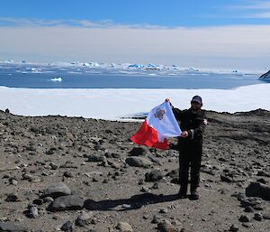 An expeditioner flying a Malta flag out on Anchorage Island, with icebergs and sea ice behind him.