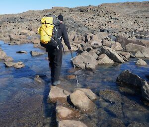 An expeditioner attempts to cross a wide area of water by balancing on rocks.