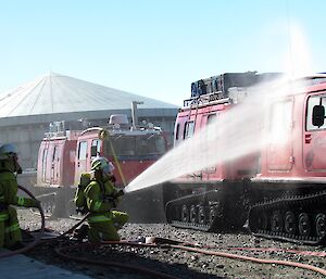 Two people in breathing apparatus are hosing down a pink Hägg in a mock fire.
