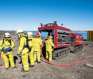 Five people in fire fighting gear are standing next to the fire truck (Hägg). Two people are in mask and breathing apparatus. The other three are working with the hoses.