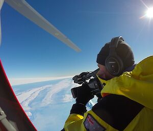 A person filming through an open door on the helicopter as it flies over Horseshoe Lake on the Sorsdal Glacier.