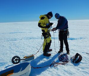 Nick is tying ropes to Tom’s safety harness as they are on crevassed ice. They are both attached to scientific equipment.