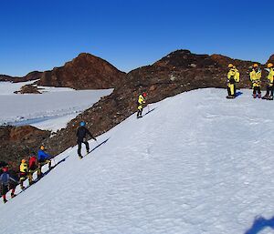 Six people are walking up a steep ice slope.
