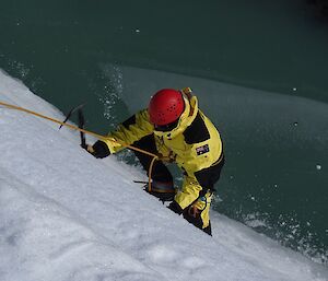 Ice climbing up the ice cliff. You can see the person is wearing crampons and using an ice axe to pull themselves up.