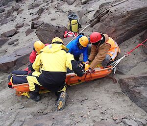 Four people are assisting with putting a patient into the stretcher during the rescue exercise.