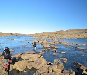 People with packs are crossing over a section of lake. Going from one boulder to another.