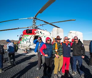 Groups of people pose for photos in front of the Kamov helicopter on the helipad.