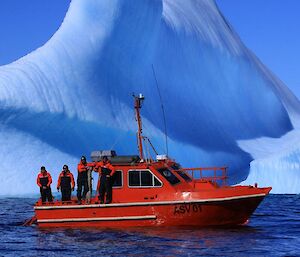 An orange work boat, called the Wyatt Earp, with four people out on deck, in front of an iceberg.