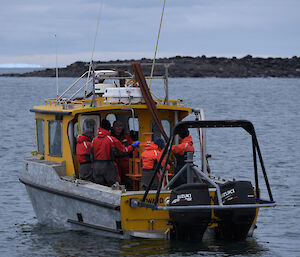 Five people are seen on the deck of the Howard Burton workboat. It is offshore of Davis. There is an island in the background.