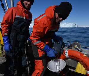 two people are collecting water samples from the boat. In the background is the Sorsdal Glacier.