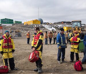 Expeditioners are standing around by the wharf in life jackets, waiting for the boat to arrive to take them to the ship.