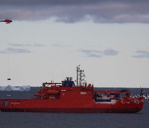 The helicopter is slinging a cage pallet of cargo onto the back deck of the ship.