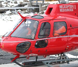 Four people are sitting in the helicopter with orange immersion suits on, about to fly out to the ship.