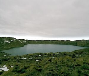 A view of Deep Lake from the rocky shoreline. The water is unfrozen and the sky is dark grey.