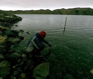 Lötter is squatting down on the lake’s edge. A short distance away from him is a pole in the lake from which you can read lake height.