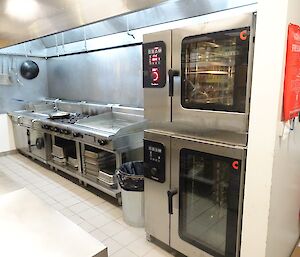Two brand new ovens are in position, stacked on top of one another. They have red lights when turned on and look fancy.
