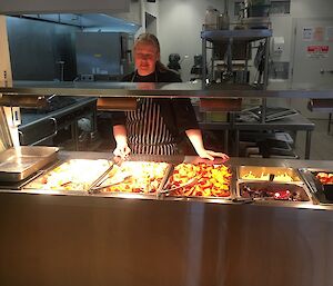 Kerryn the chef is standing in the kitchen behind the bain marie which is full of delicious food.
