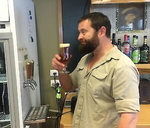 Marc is standing in the bar having just poured himself a draught beer that he made. He has a big smile on his face as he is about to take his first sip.