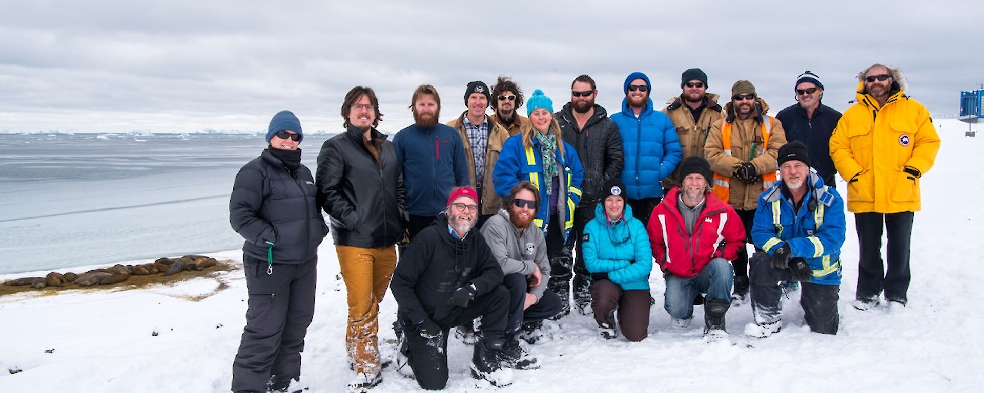 The winter team back row (L-R): Kirsten, Ralph, Sharky, Rob, Lotter, Kerryn, Marc, Bryce, Jock, Tony, Barry B2, Fitzy; front row: Barry B1, Shoey, Daleen, Rhys and Richard. In the background are the resident elephant seals and newly formed sea-ice in the bay.