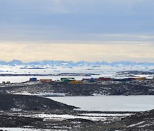 A view from the top of The Lookout. There are brown hills amongst the ice, with colourful buildings in the distance. Behind the station are icebergs on the horizon.