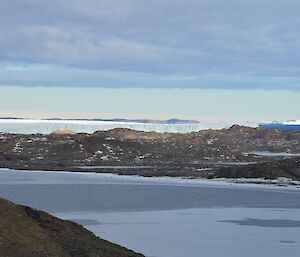 In the distance, behind the fjord and hills, lies a large glacier. This is the face of the Sørsdal Glacier.