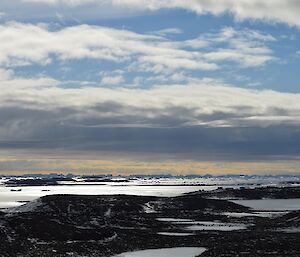 The Vestfold Hills are in the foreground while many, many icebergs are out in the ocean on the horizon, under a beautiful blue sky.