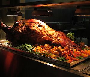 The delicious dinner of a whole spit roast lamb, surrounded by roasted vegetables.