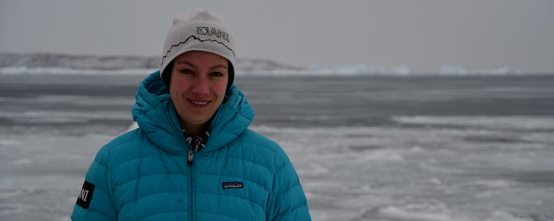 Daleen is wearing a blue puffer jacket, smiling at the camera. Sea-ice is in the background.