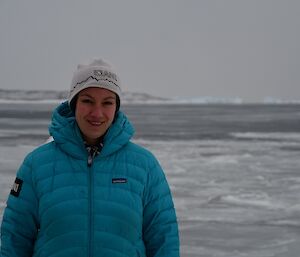 Daleen is wearing a blue puffer jacket, smiling at the camera. Sea-ice is in the background.