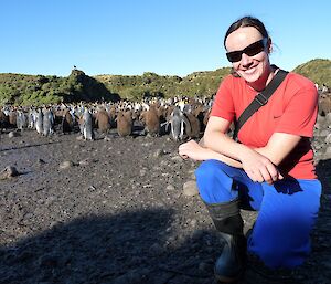 Daleen is crouching in front of some adult and chick king penguins at the sub-antarctic Marion Island. Tussock grass is also seen in the background.