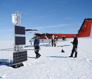 At the end of the work, everyone is standing around smiling. Lotter is taking video of the AM06 equipment. Nick is having a hot drink. In the background Marc and Doug are loading equipment into the Twin Otter plane.