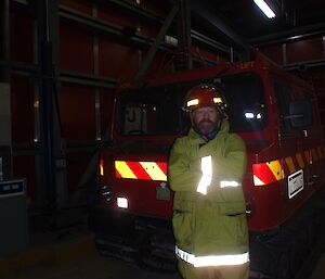 Fitzy is wearing protective fire fighting clothing and is standing in front of the fire truck Hagg.