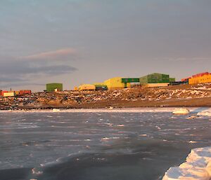 Thin, grey, new sea-ice is seen in the bay offshore of Davis. The buildings are up on the hill behind the beach.