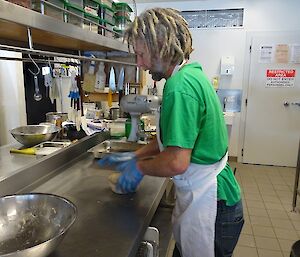 Rhys is in the kitchen, wearing an apron, kneading his hotcross bun dough out on the bench.