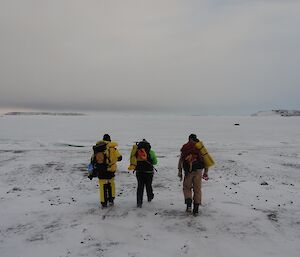 Heading out on a walk over the seaice to Gardener Island. Three people are carrying backpacks and dressed in outdoor gear.