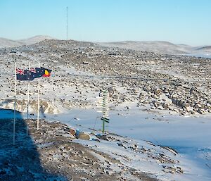 The flags flying at full mast on ANZAC Day at Davis. In the background are snow covered hills.