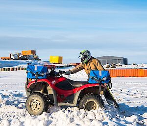 Robert’s bike is bogged in the snow. He is beside the bike, lifting the rear and attempting to accelerate it forward to get it out of the snow.