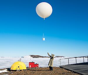 A weather balloon is released from the back of the Met building. The Met staff is dressed in protective clothing for the activity.