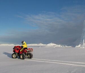 Ralph is sitting on a quad bike which is stopped near an iceberg parked in the seaice.